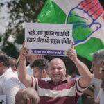 Crowd holding a political banner with a flag at a demonstration in India.