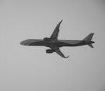 A monochrome image of a commercial airplane flying high in the clear sky.