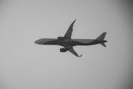 A monochrome image of a commercial airplane flying high in the clear sky.